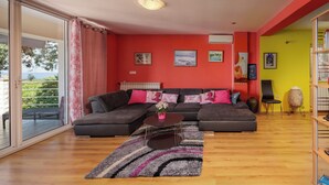 A living room with a sectional sofa, a coffee table, and a large window with a view of greenery. - Colourful Seaview Apartment (Kostrena)