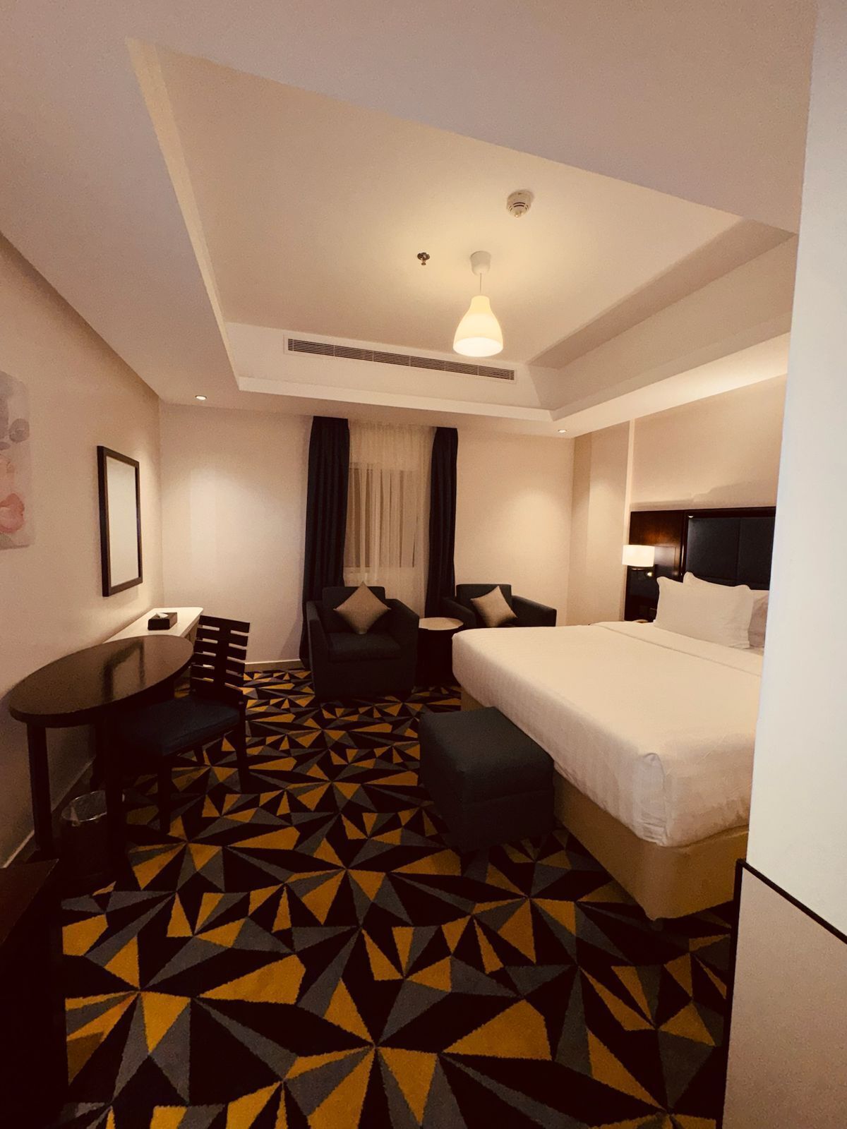 A hotel room with a bed, two armchairs, a small table, and a patterned floor.