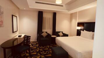 A hotel room with a bed, two armchairs, a small table, and a patterned floor.