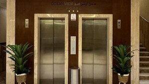An elevator entrance at Ocean View Hotel with two elevators, a trash bin, and potted plants. - Ocean View Al Zahra (Jeddah)