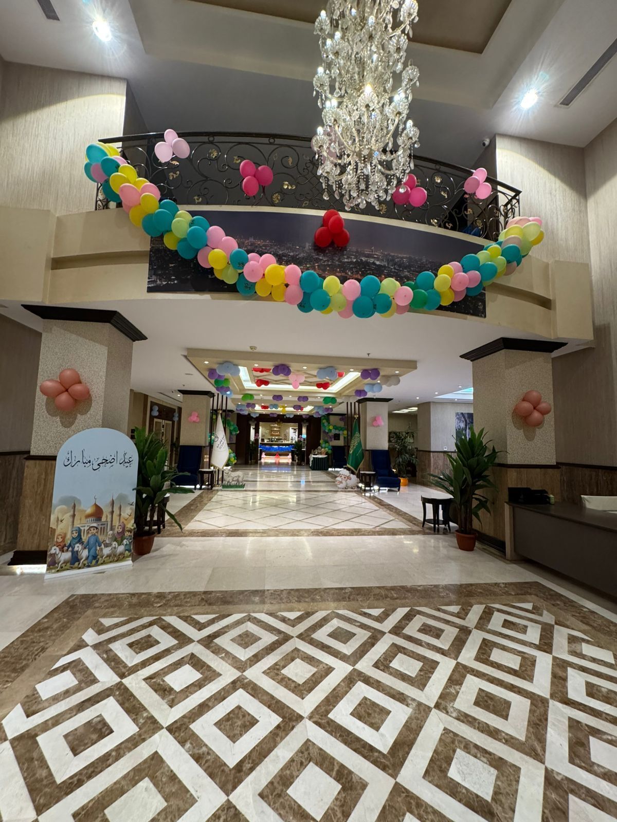 Un vestíbulo de hotel con una araña, decoraciones de globos de colores, un suelo estampado y una mesa de recepción.
