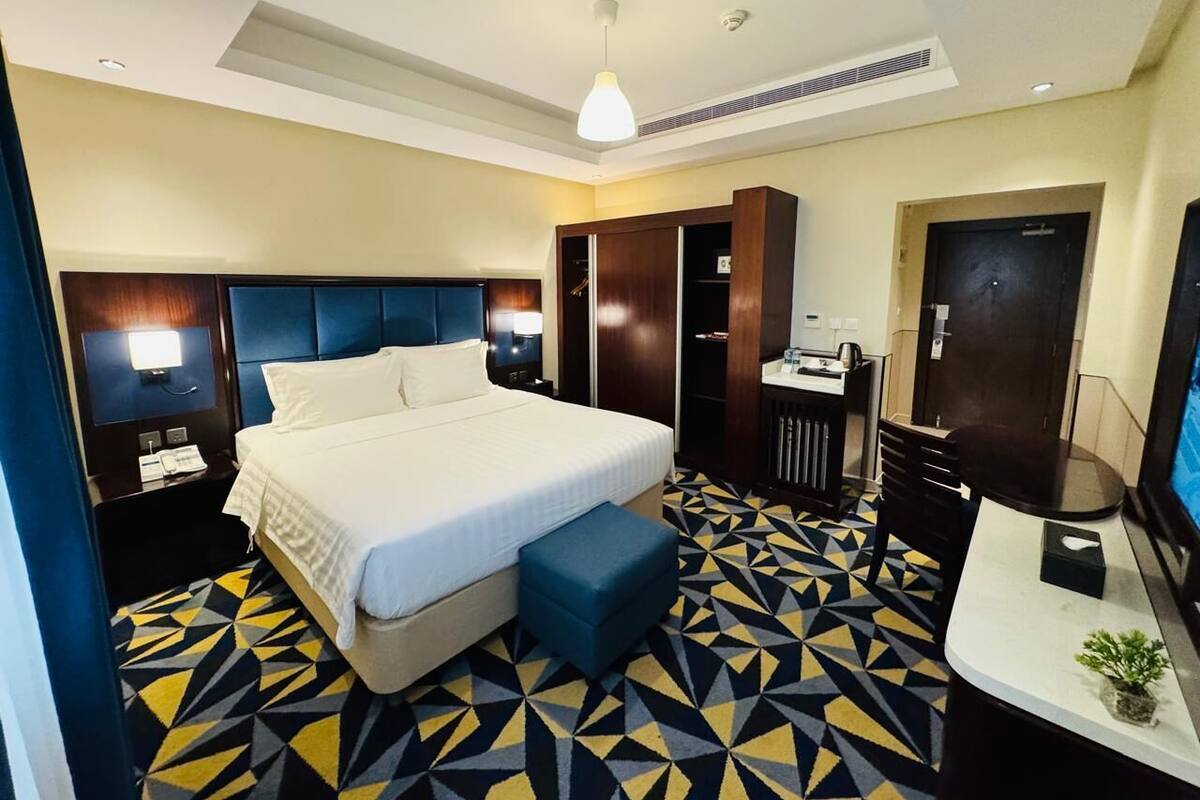 Quarto de hotel com cama, escrivaninha, cadeira, televisão e banheiro.