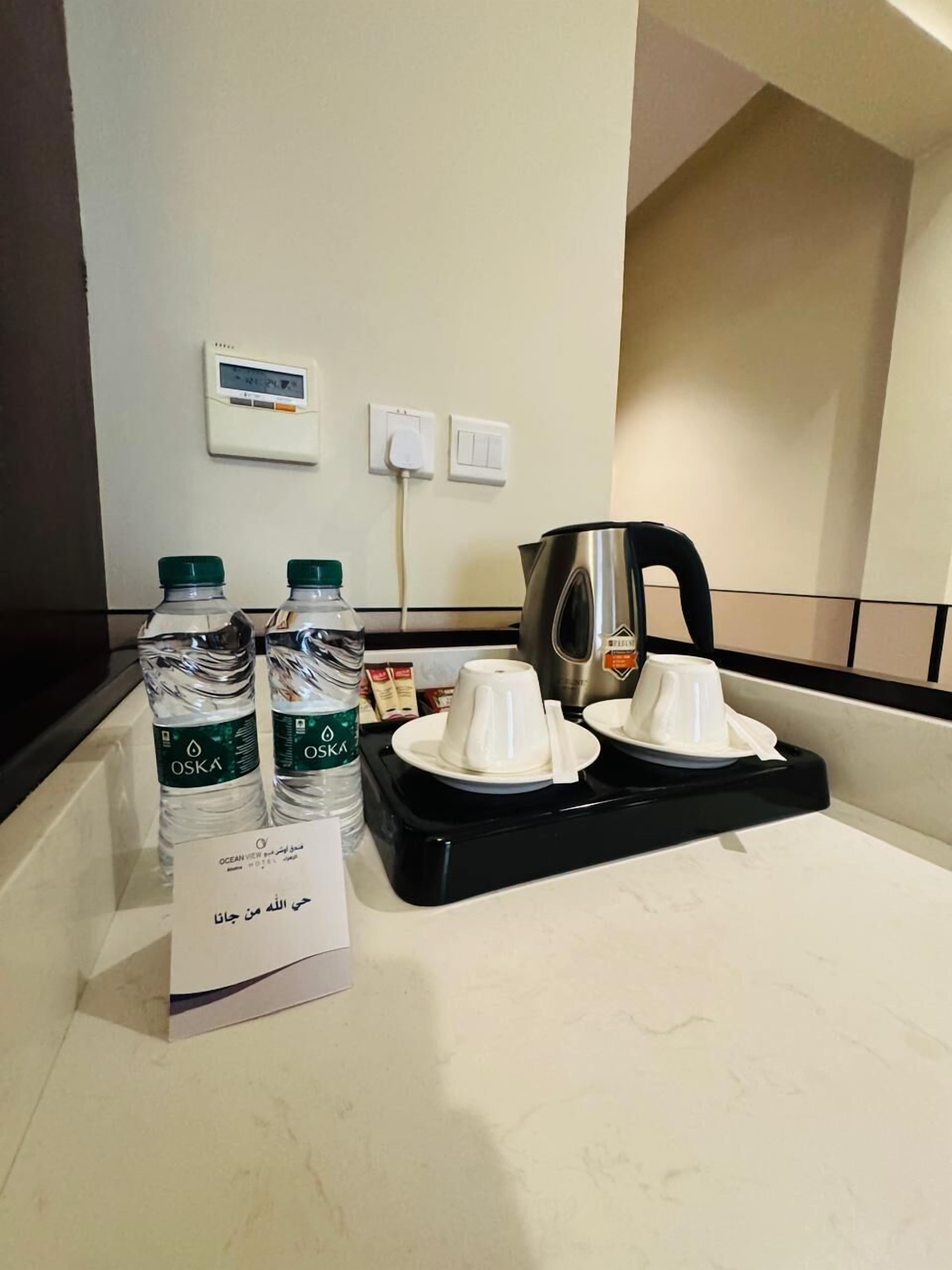 A hotel room counter with two water bottles, a coffee maker, and a sign with Arabic text.