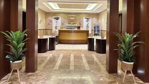 A reception area with a coffee shop counter, two receptionists, and potted plants. - Ocean View Al Zahra (Jeddah)