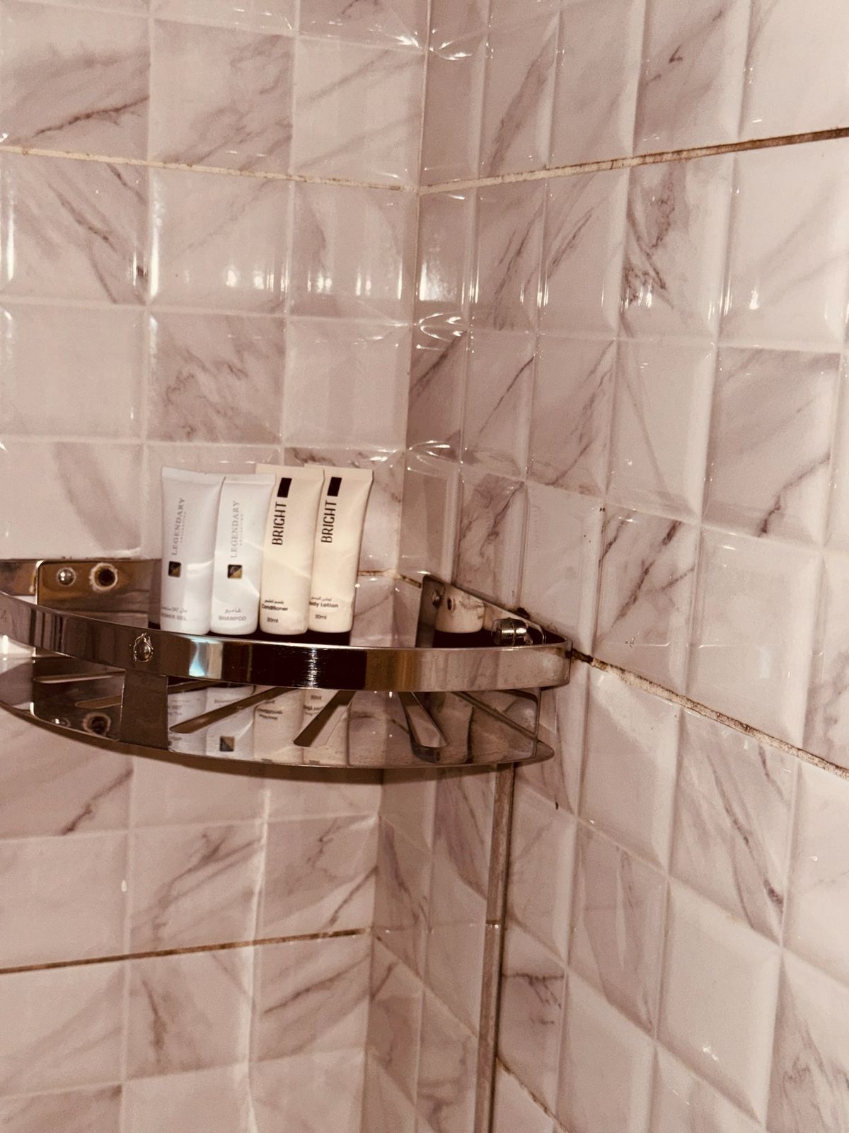 Une salle de bain carrelée de marbre, une étagère en verre où sont rangés les articles de toilette, et un robinet chromé.