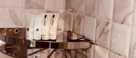 Une salle de bain carrelée de marbre, une étagère en verre où sont rangés les articles de toilette, et un robinet chromé.