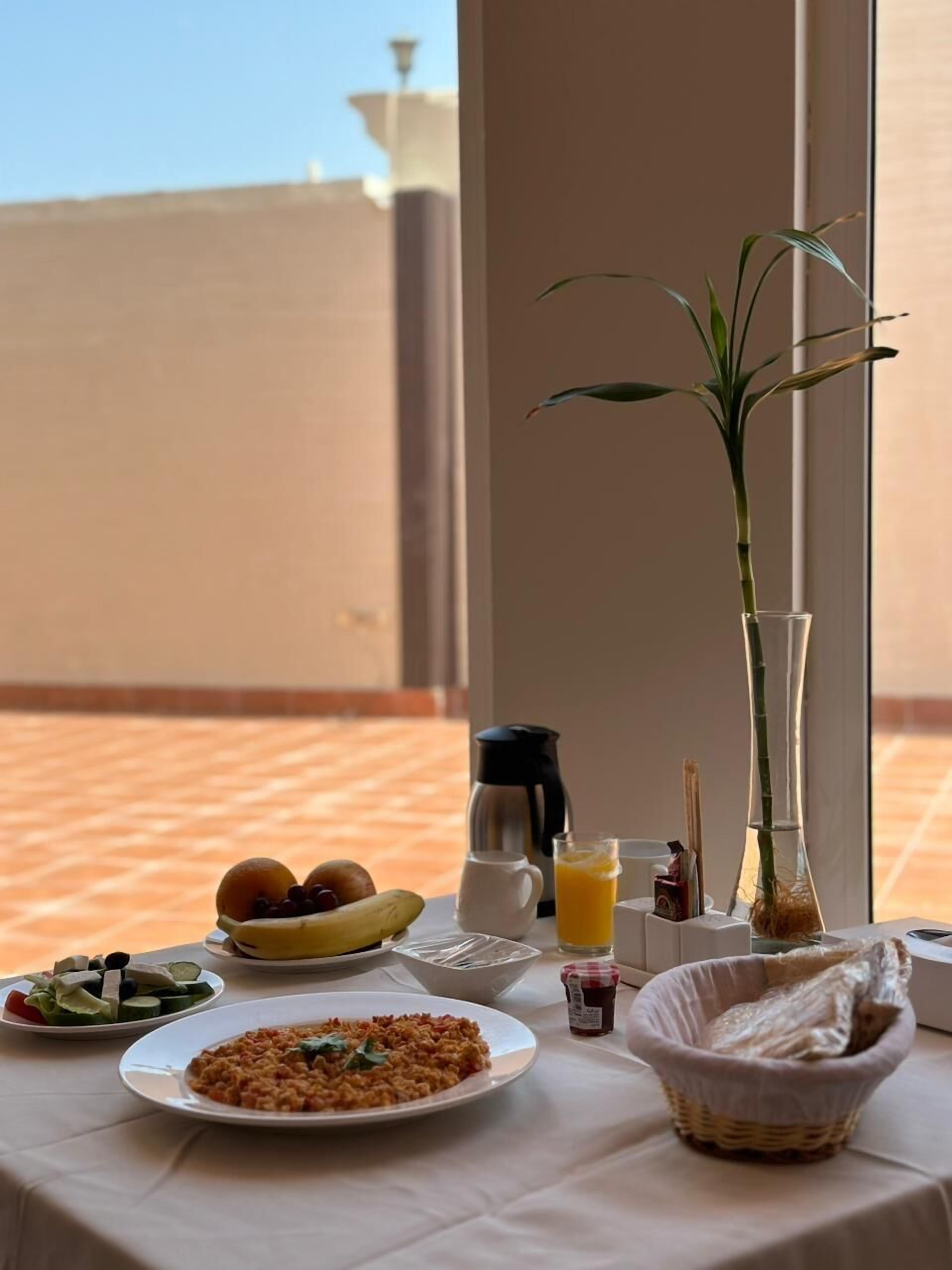 A breakfast table with plates of food, a coffee pot, a glass of orange juice, and a vase with a plant.