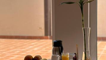 A breakfast table with plates of food, a coffee pot, a glass of orange juice, and a vase with a plant.