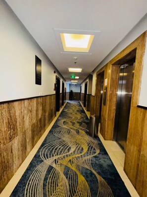 Un pasillo de hotel con alfombra estampada, puertas y un acceso a un ascensor.