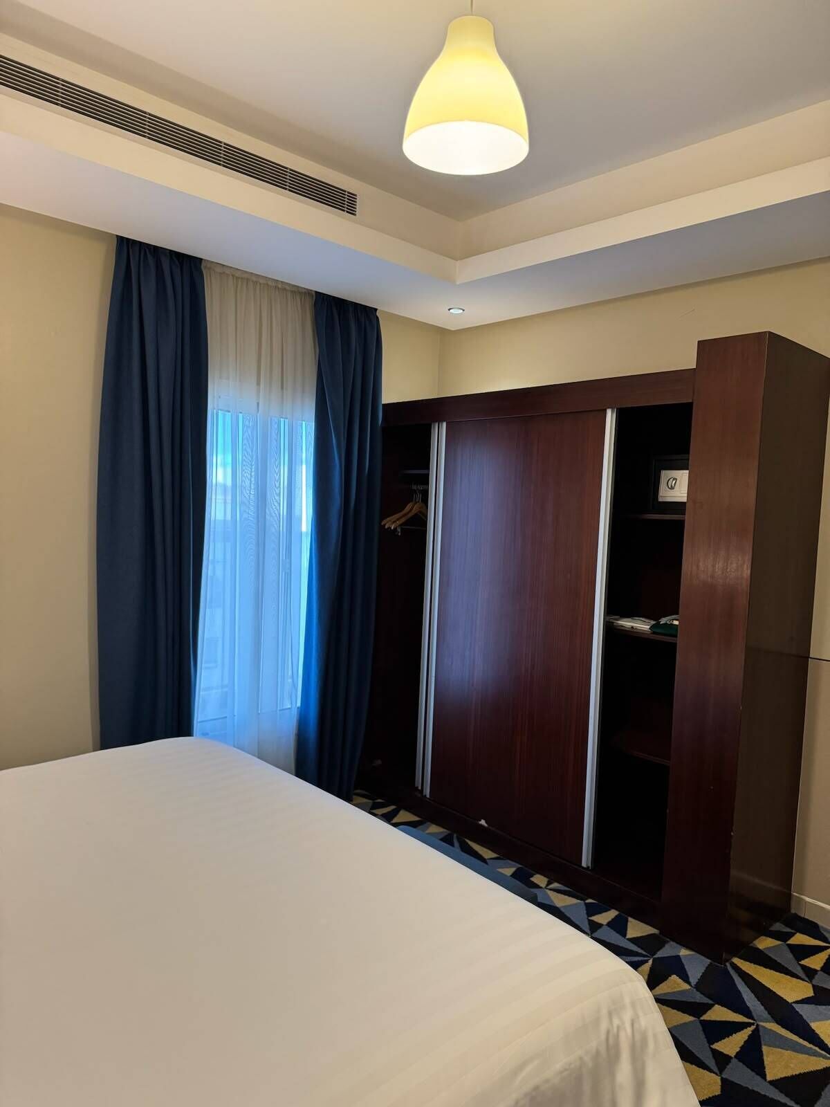 Une chambre d’hôtel avec un lit, une armoire, un placard et un sol à motifs.