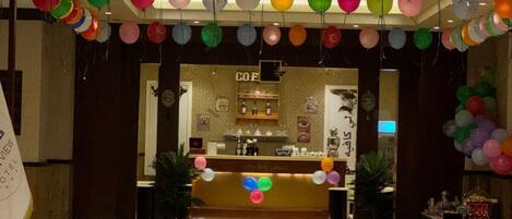 En hotellobby med en receptionsdisk, ett kafé och färgglada ballonger.