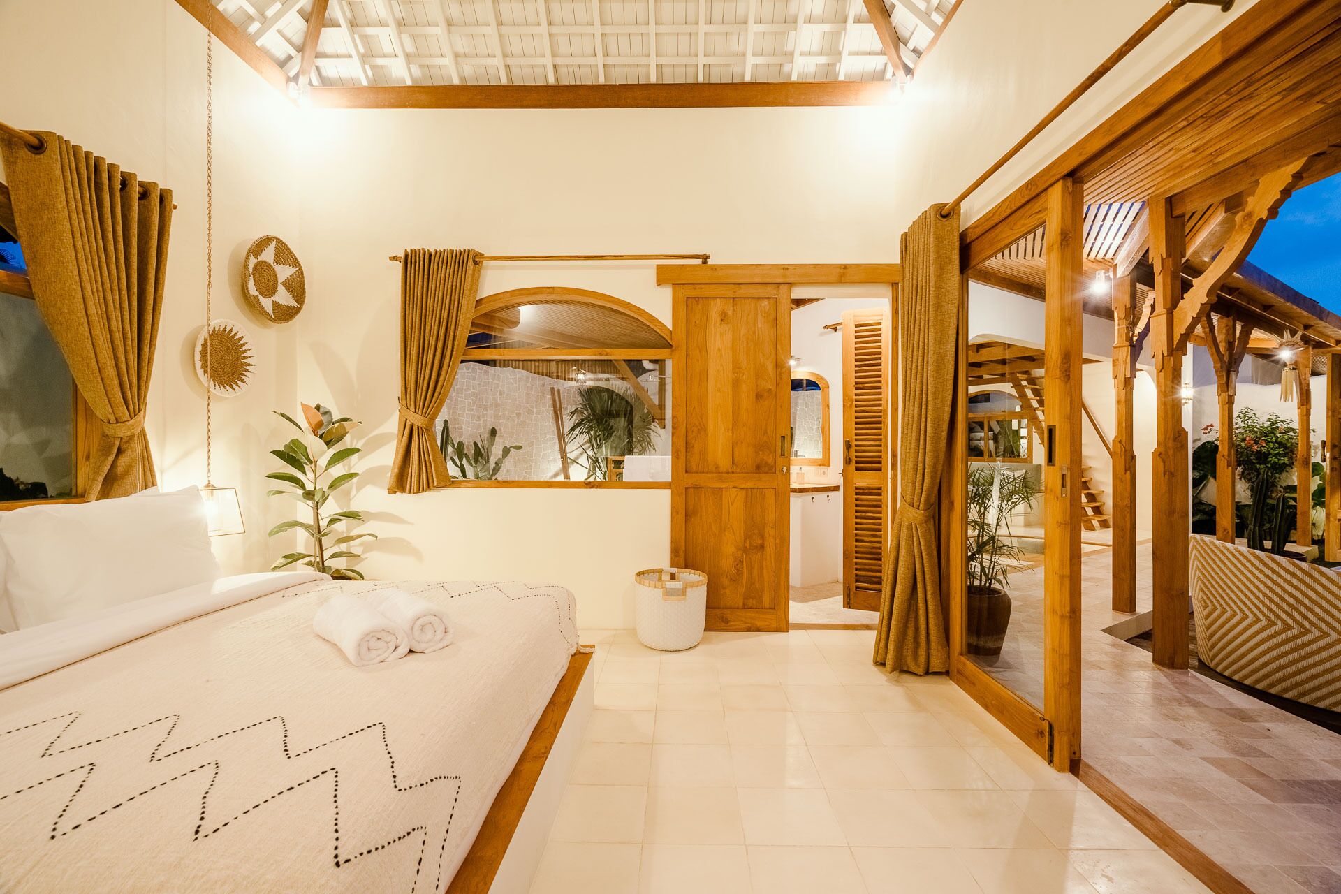 Une chambre spacieuse avec un grand lit, une porte en bois donnant sur un balcon et une vue sur l’extérieur.