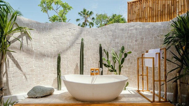 A spa area with a large white bathtub, a wooden bench, and a wooden fence. - Canggutopia by Alfred in Bali (Canggu)
