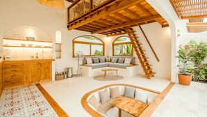A spacious living area with a wooden staircase, a kitchen with a built-in island, and large windows providing natural light. - Canggutopia by Alfred in Bali (Canggu)