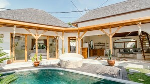 A poolside area with a covered patio, a seating area, and a kitchen visible through an open archway. - Canggutopia by Alfred in Bali (Canggu)