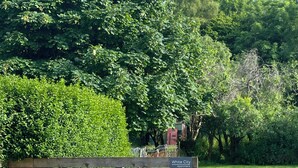 A wooden deck with a table and chairs, surrounded by a well-maintained lawn and dense greenery. - The White City Apartment (Oban)