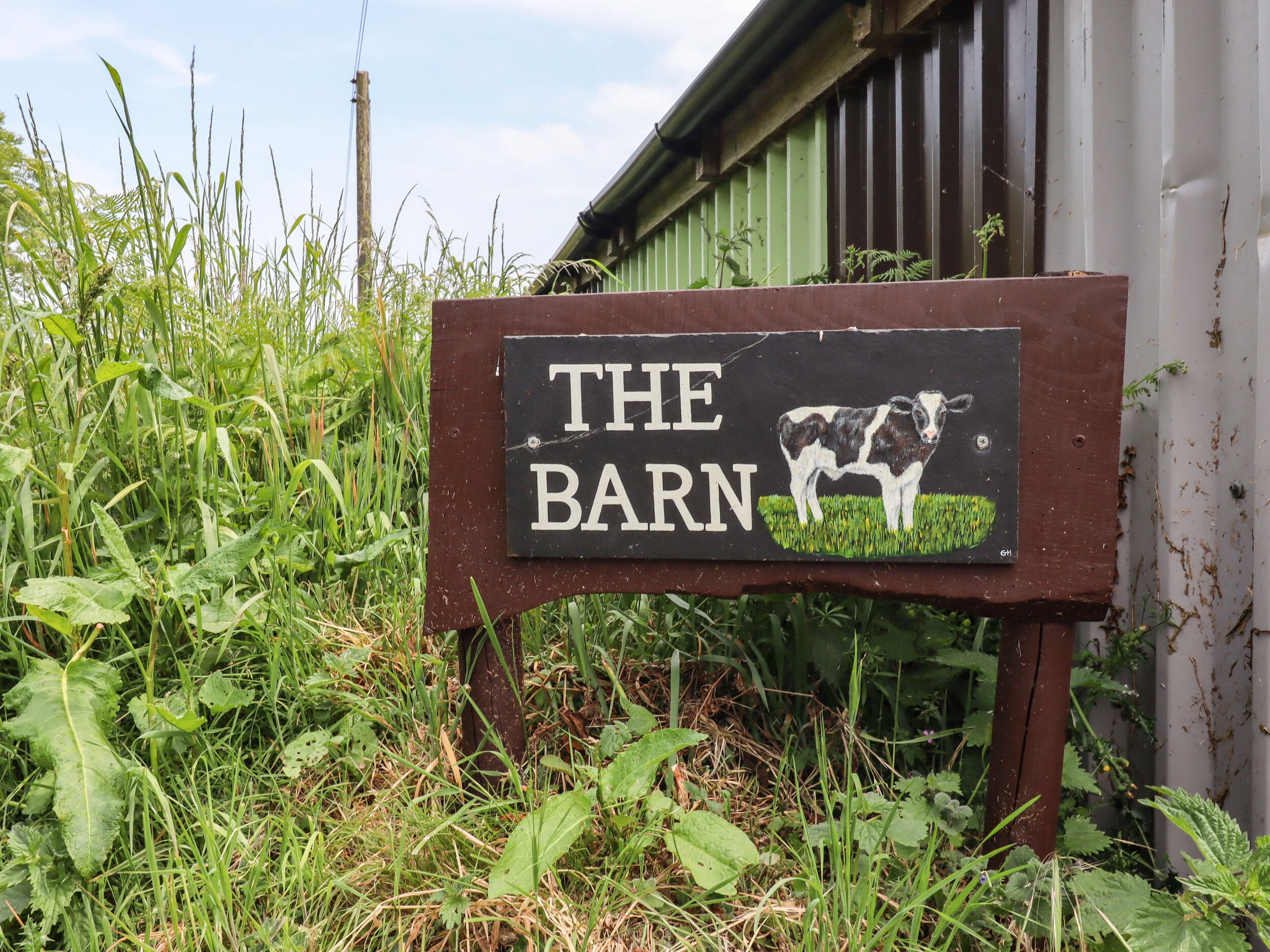 A rustic sign with "THE BARN" and a cow illustration, surrounded by greenery.