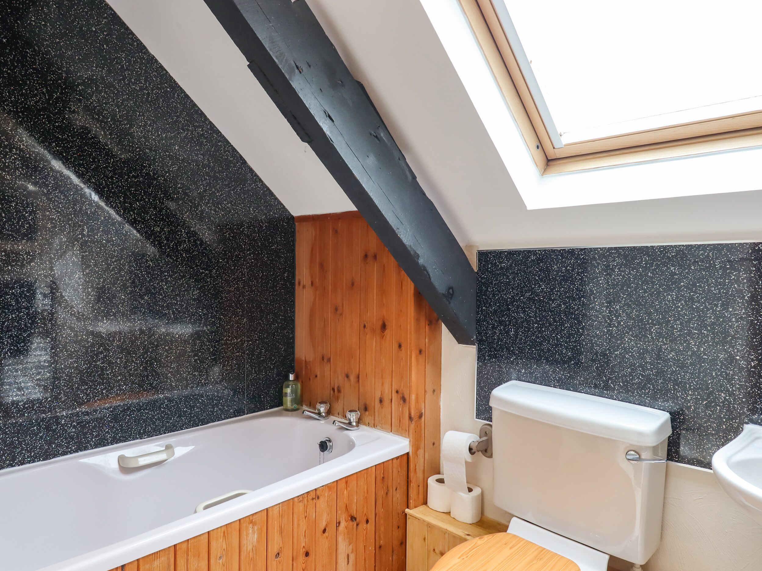 A bathroom with a skylight, a bathtub, a toilet, and wooden paneling.
