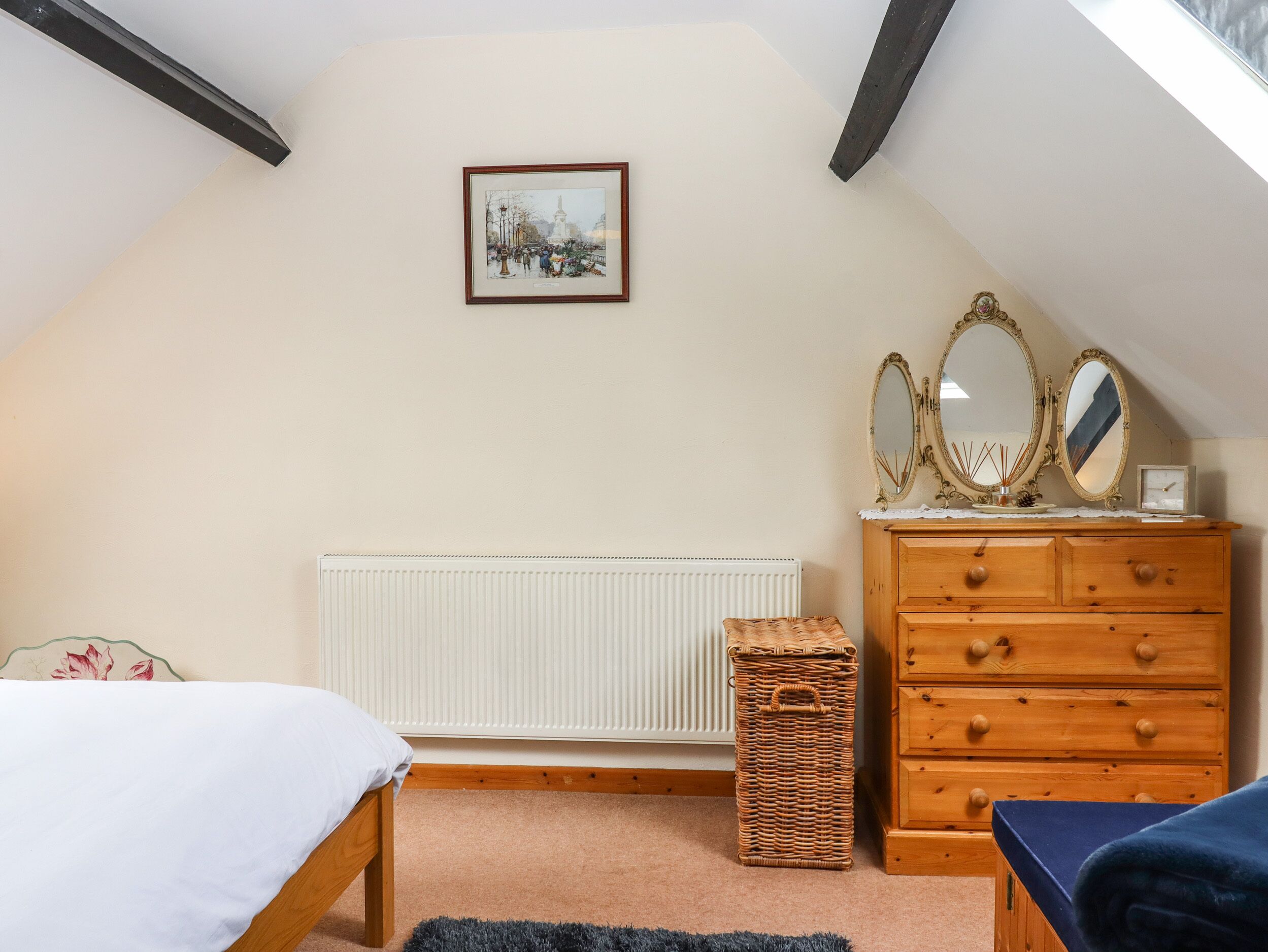 A bedroom with a bed, a dresser with mirrors, a radiator, and a framed picture on the wall.
