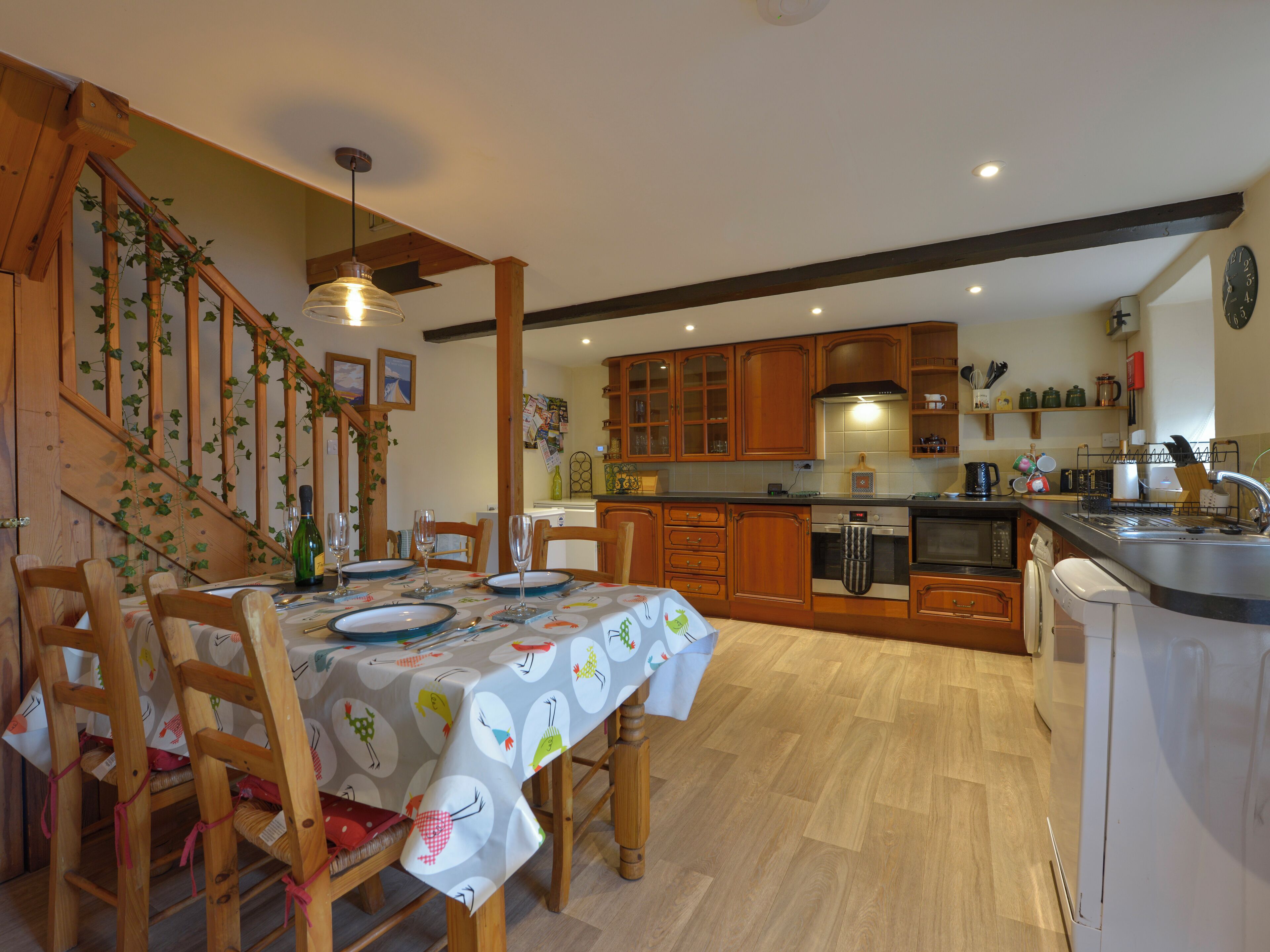 A kitchen with wooden cabinets, a dining table with chairs, and a staircase with climbing plants.