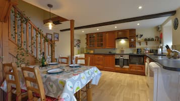 A kitchen with wooden cabinets, a dining table with chairs, and a staircase with climbing plants.