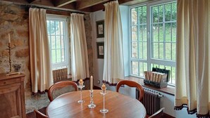 Ein Essbereich mit einem runden Holztisch, zwei Stühlen, einem Kerzenhalter und einem Fenster mit Vorhängen.