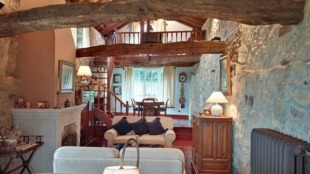 Ein rustikales Interieur mit Steinwand, Holzbalken, einer Treppe, einem Kamin und einem Essbereich.