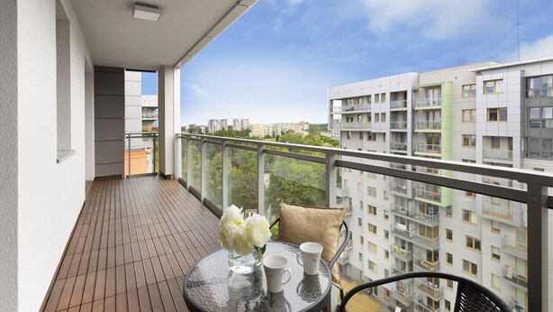Een balkon met een tafel, stoelen en een bloevas.