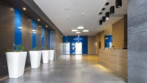 Een moderne hotel lobby met een lange receptiebalie, betegelde vloer en potplanten.