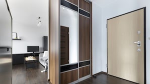 Een moderne kamer met een schuifdeurkast van hout, een gesloten deur, een flatscreen televisie, een bank en een klein tafeltje.