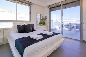Ein modernes Schlafzimmer mit einem großen Bett, einem Nachttisch, einer Lampe und Blick auf den Balkon.