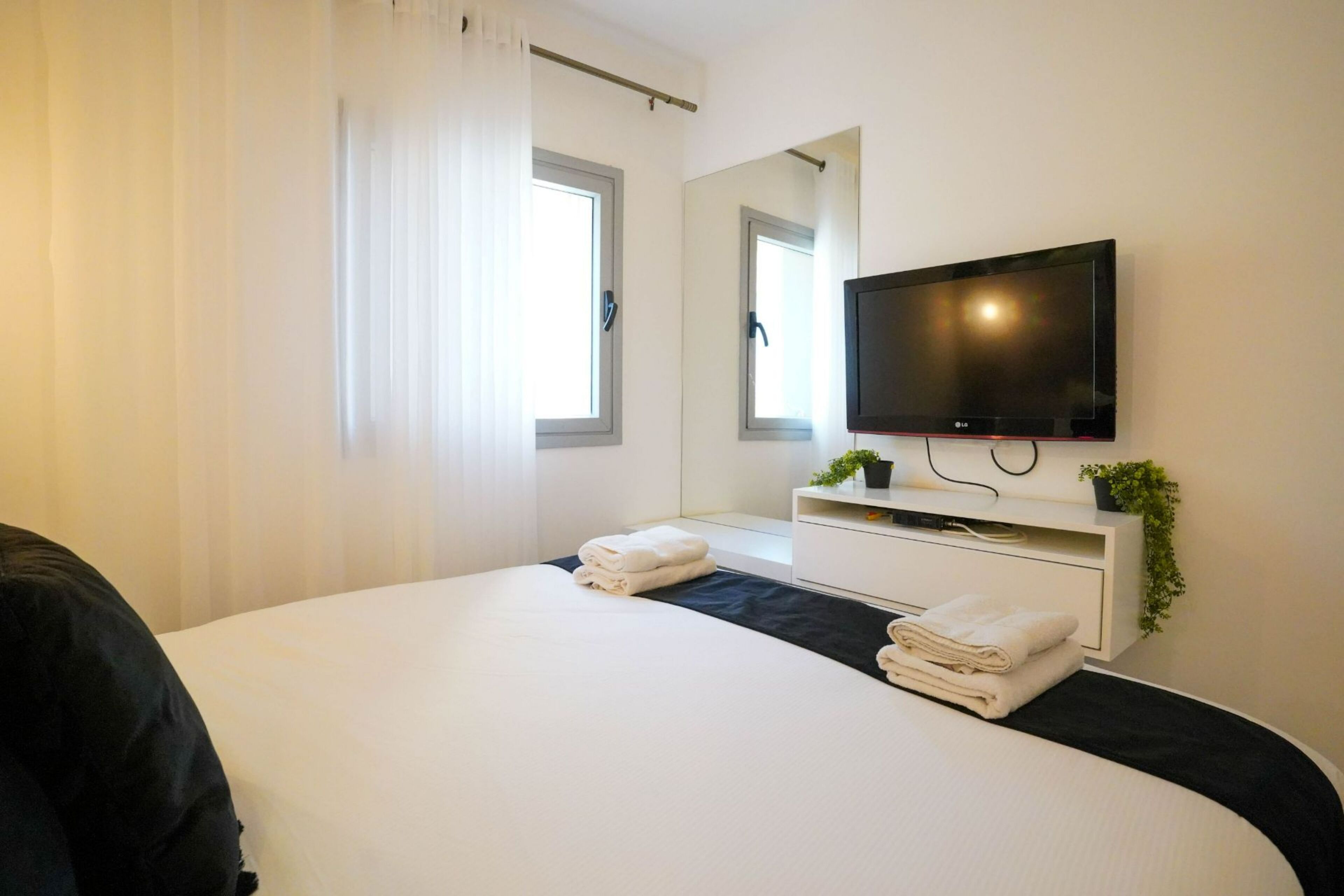 Una habitación de hotel moderna con una cama grande, un televisor de pantalla plana, un escritorio pequeño y un ventanal con cortinas.