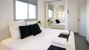 Moderni hotellihuone, jossa on suuri sänky, peili ja ikkuna.