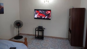 Ein Zimmer mit einem Bett, einem an der Wand montierten Fernseher, einem Ventilator, einem Schrank und gefliestem Boden mit Muster.