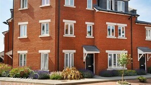 A multi-story brick building with white-framed windows, a flat roof, and a small garden area with plants and a tree. - Admiral's Quarter Apartment 5 (Weymouth)