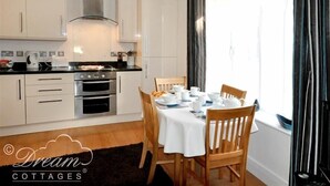 A modern kitchen with white cabinets, a stove, and a dining area with a table set for four. - Admiral's Quarter Apartment 5 (Weymouth)