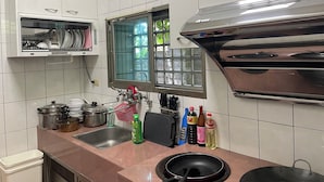 Une cuisine avec des murs recouverts de carreaux blancs, un évier en acier inoxydable, une fenêtre donnant sur un beau paysage et une horloge au mur.