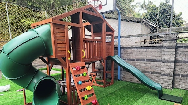 Une structure de jeu en bois comprenant un toboggan, un mur d’escalade et un panier de basket.