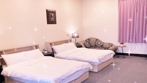 Une chambre d’hôtel avec deux lits, un canapé, une petite table et un luminaire au plafond.