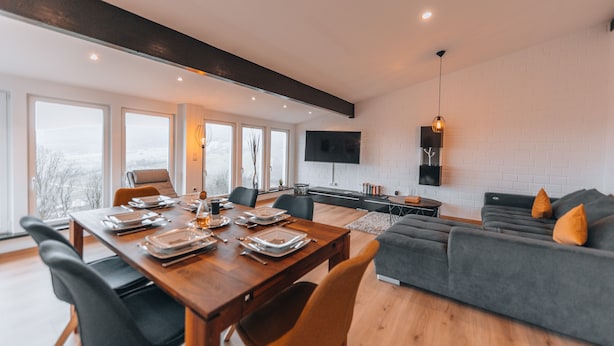 A modern living space with a dining area, a sofa, and a TV mounted on the wall. - RhönKristall modern terrace house with a far-reaching view (Bischofsheim in der Rhön)