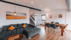 A modern living room with a sectional sofa, a wooden coffee table, and a dining area with a wooden table and chairs. - RhönKristall modern terrace house with a far-reaching view (Bischofsheim in der Rhön)