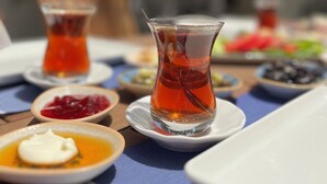 Ein Tisch, reichhaltig gedeckt mit verschiedenen Speisen und Getränken, darunter eine Teekanne, Schüsseln mit Essen und ein Teller.