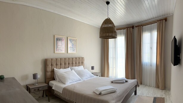 Ein Schlafzimmer mit einem großen Bett, einem Nachttisch, einer Lampe, einer Pendelleuchte und einem Fernseher an der Wand.