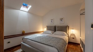 A bedroom with a bed, a skylight, a nightstand, a lamp, and two framed pictures on the wall. - Le terrazze nel cuore della Kalsa by Wonderful Italy (Palermo)