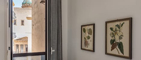 A hotel room with a balcony, a bed, a nightstand, and two framed botanical prints on the wall.