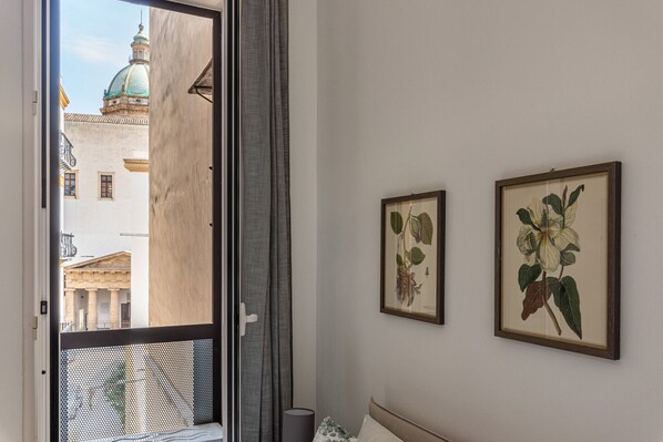A hotel room with a balcony, a bed, a nightstand, and two framed botanical prints on the wall.