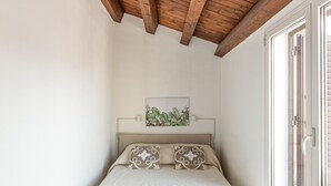 A bedroom with a wooden ceiling, a bed with a white quilted bedspread, a headboard with a plant, and a view through a glass door. - Casa Brunaccini con Terrazza by Wonderful Italy (Palermo)