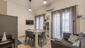 A modern living room with a sofa, a dining table with chairs, a TV mounted on the wall, and a window with curtains. - Casa Brunaccini con Terrazza by Wonderful Italy (Palermo)