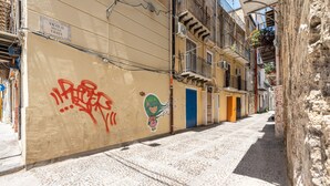Un vicolo stretto con un edificio caratterizzato da una porta blu e una targa che riporta la scritta 'Vicolo delle Travi'.