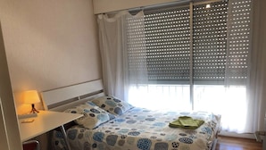 Ein Schlafzimmer mit Bett, Schreibtisch, Stuhl und einem Fenster mit Jalousien.